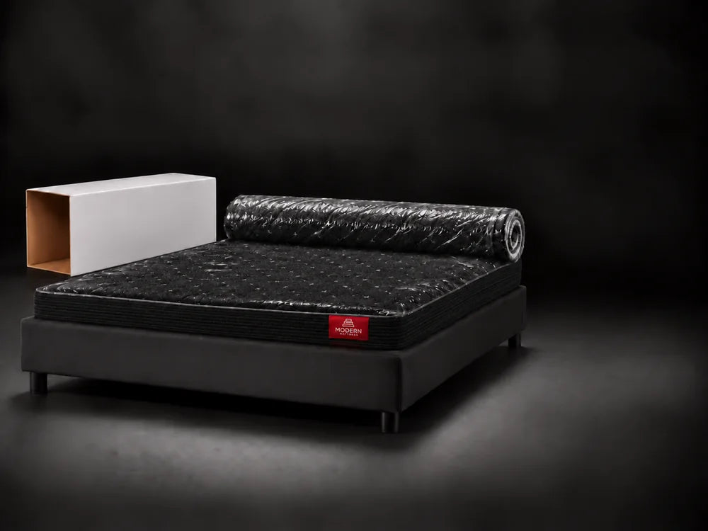 The black Luna half unrolled on the bed base, still in its plastic
